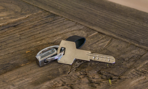 A silver key with a black plastic head lies on a rustic wooden table. The weathered wood's texture contrasts with the key's smooth surface.
